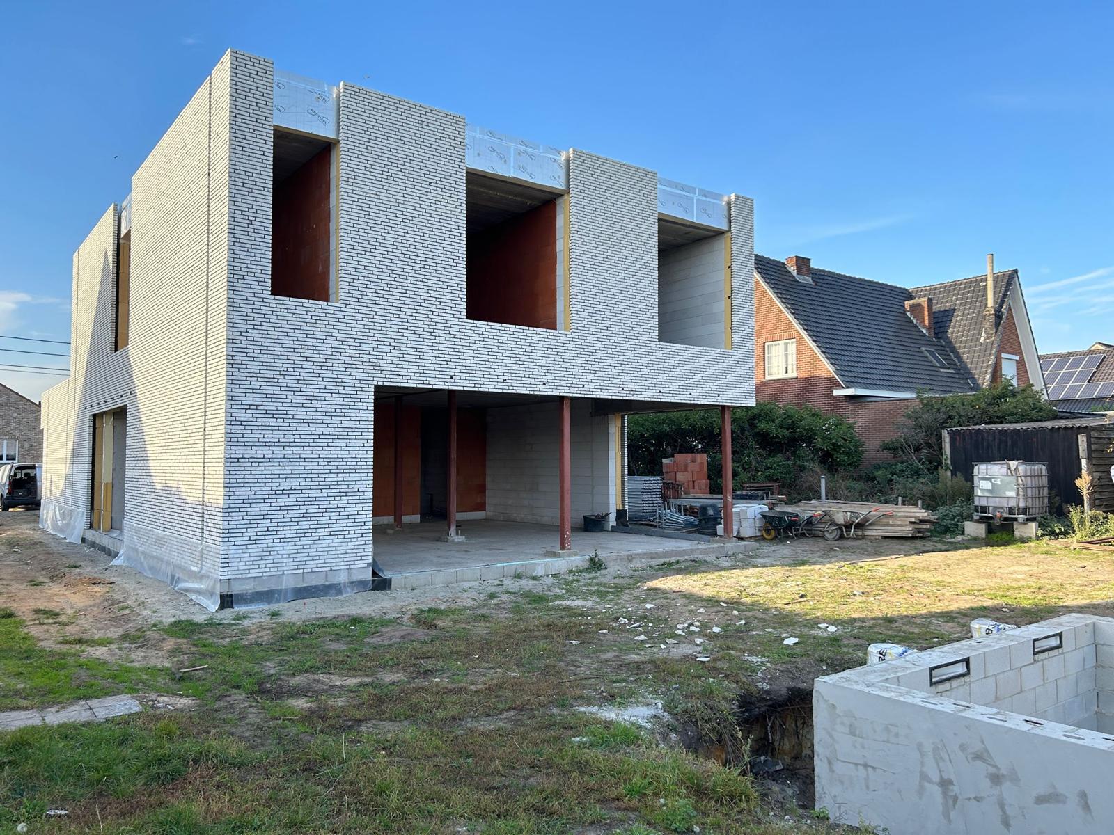 Moderne nieuwbouwwoning in witte baksteen met grote raamopeningen tijdens ruwbouwfase