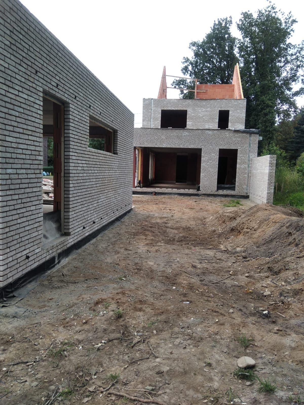 Zicht op werf met bijgebouw en hoofdvolume in lichtgrijs metselwerk