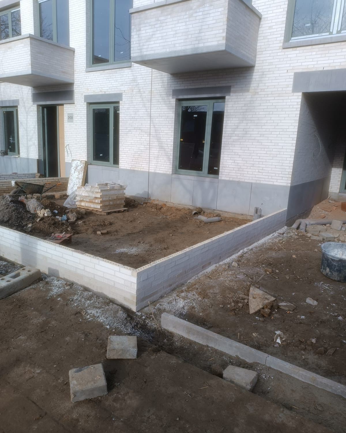Werf tijdens ruwbouwfase: metselwerk tuinmuur en betonnen dorpels bij nieuwbouwappartementen