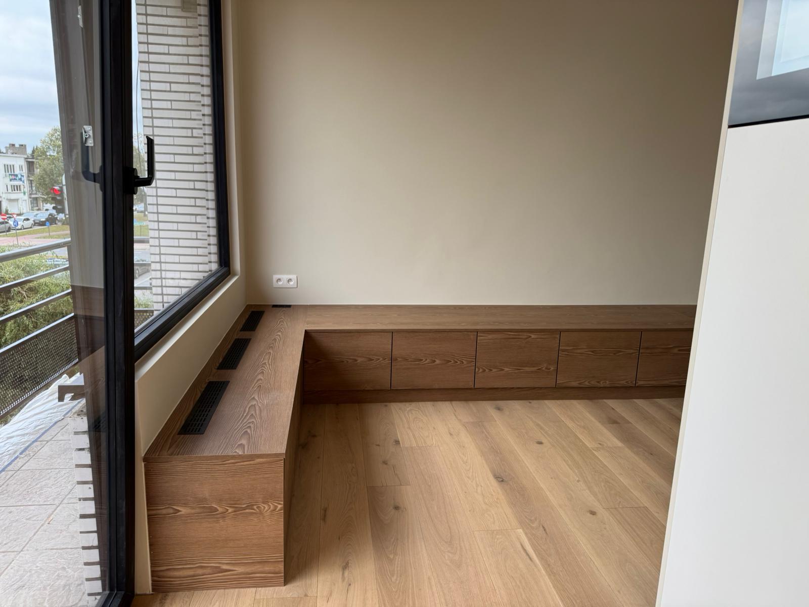 Zithoek met maatwerk eiken bankmeubel aan raampartij in afgewerkt nieuwbouwappartement