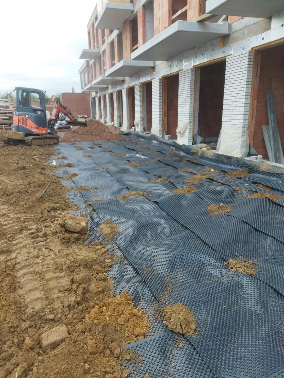Rij nieuwbouwwoningen in ruwbouwfase met betonnen terrasplaten en noppenfolie langs de kelderwand — ruwbouw door IMW Building