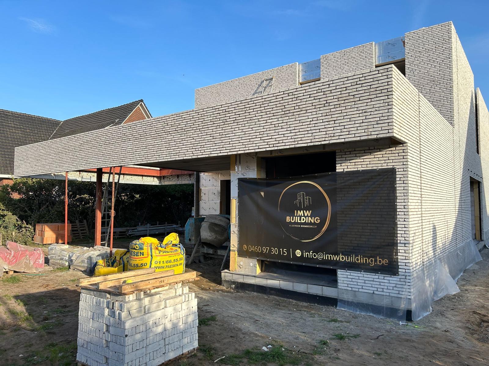 Nieuwbouwvilla in lichtgrijze baksteen met betonnen luifel en IMW Building werfbanner op de gevel