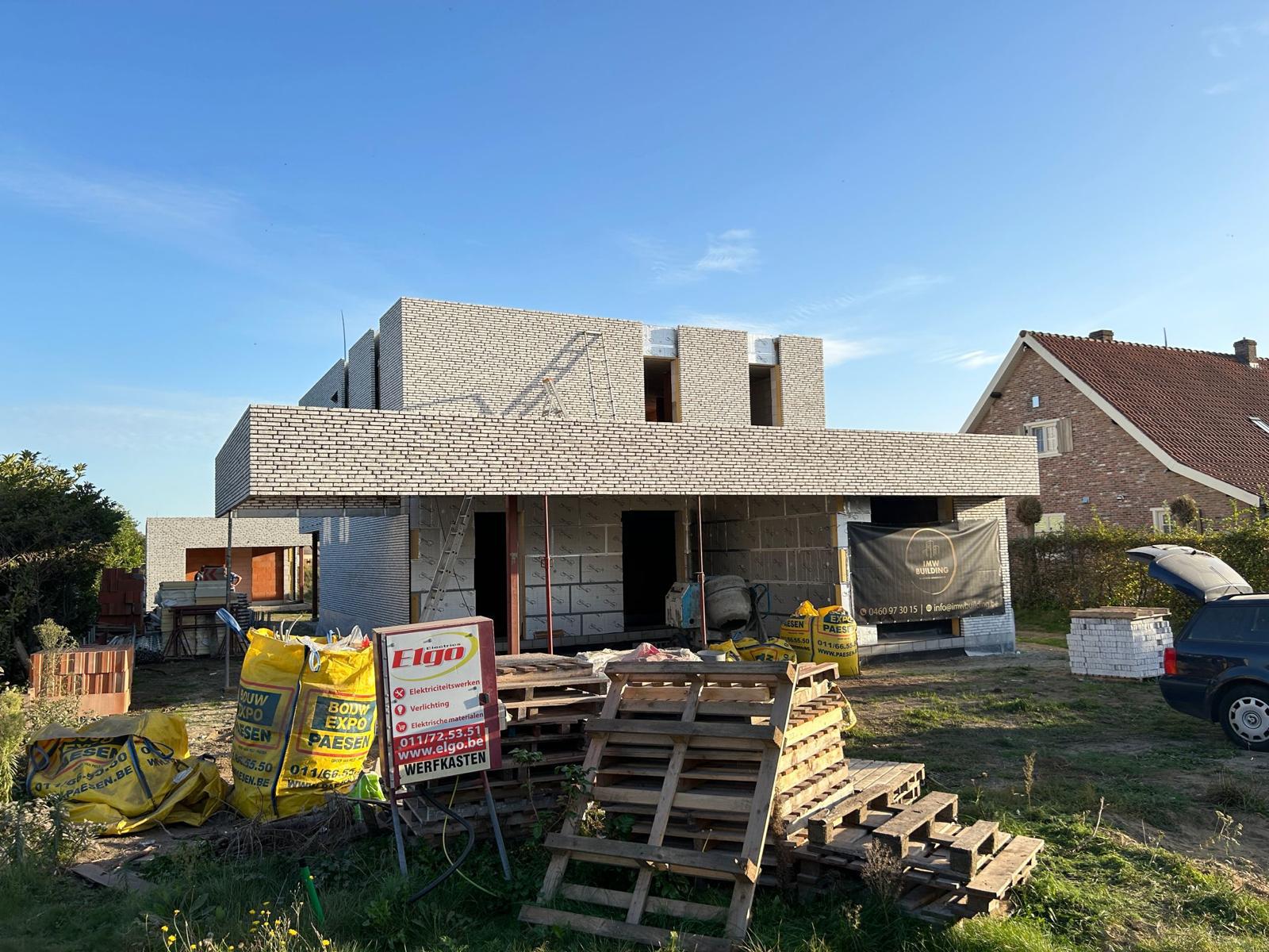 Nieuwbouwwoning met bijgebouw in lichte baksteen tijdens ruwbouwfase met werfmateriaal