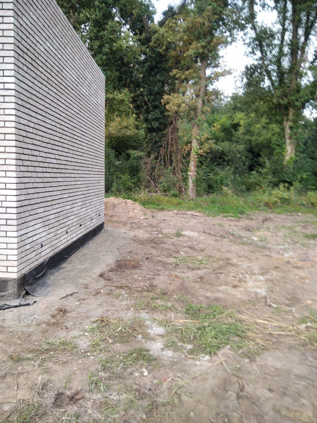 Blinde gevel in lichtgrijze baksteen met waterdichting aan de voet