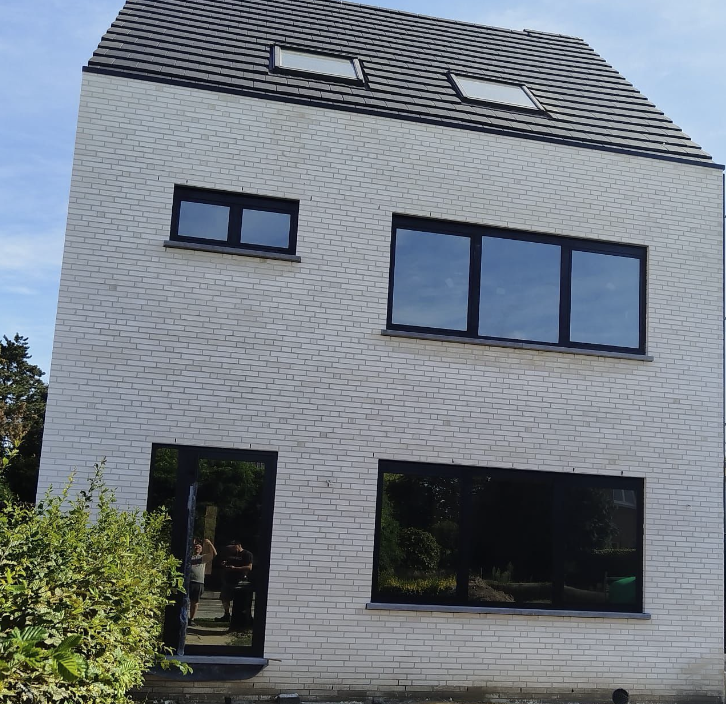 Afgewerkte gevel in lichtgrijze baksteen met zwart schrijnwerk en dakvlakramen