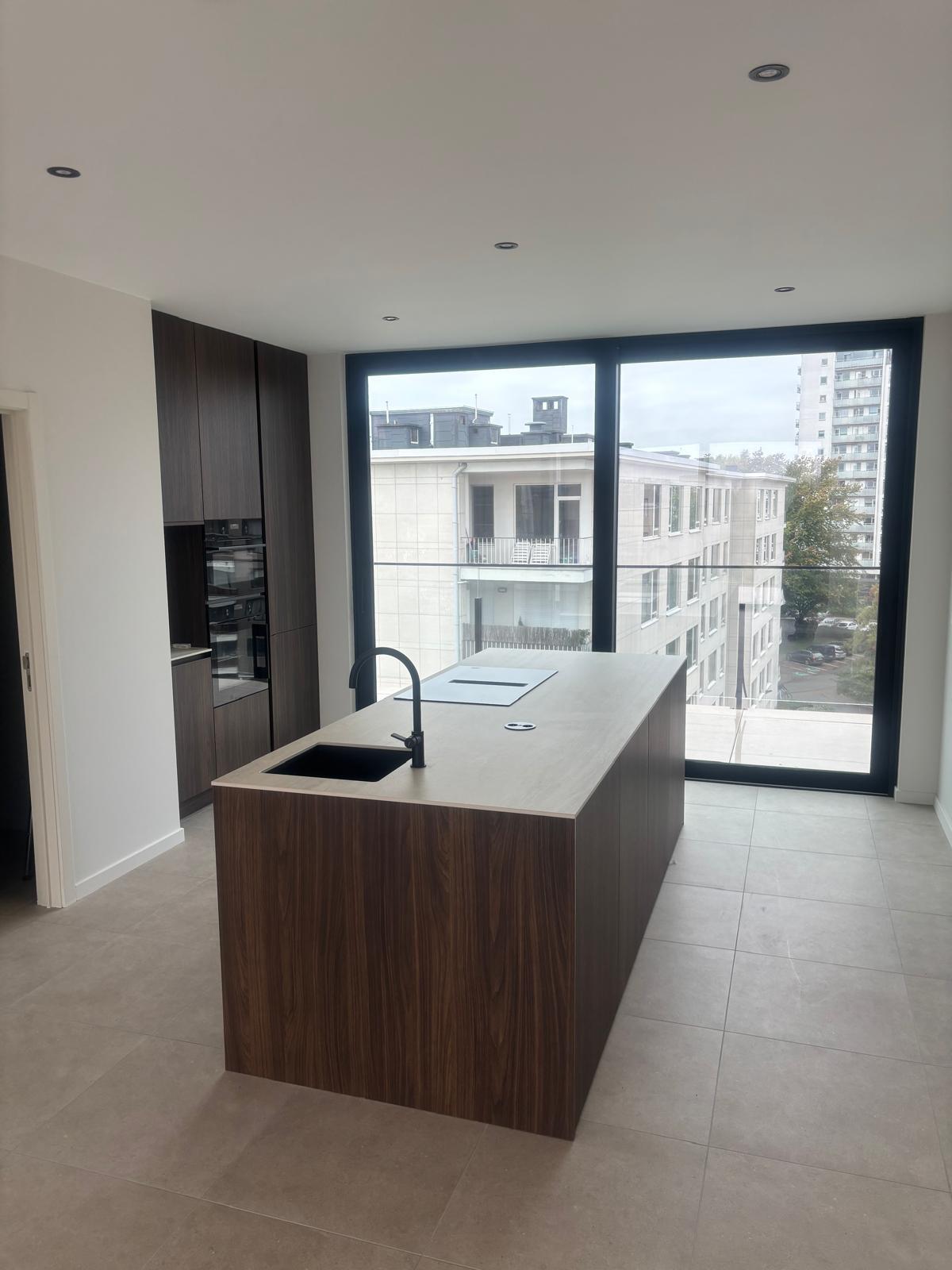 Afgewerkt appartement met maatwerkkeuken in donker hout en volledig glazen gevel — oplevering door IMW Building
